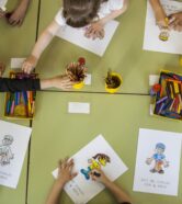 overhead view of several primary school children overhead view of several primary school children making a picture with paintings on their class table at school